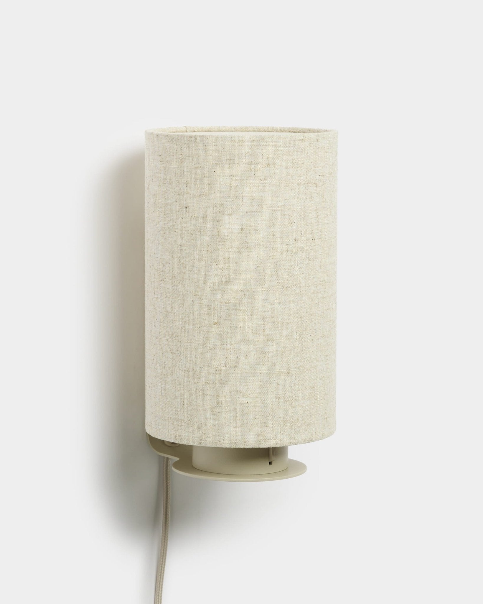 Feya | Wall Lamp de WoodUpp con pantalla cilíndrica de lino y algodón y cable blanco visible, acabado beige, diseñada para complementar los paneles acústicos de madera.